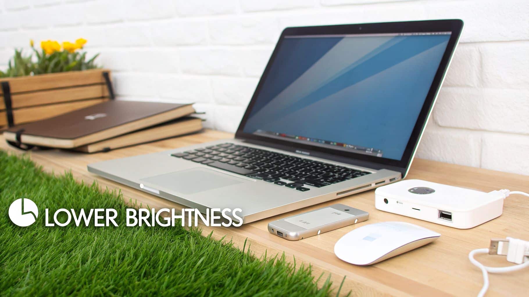 A laptop on a wooden desk with a 'Lower Brightness' logo, illustrating tips for extending battery life.