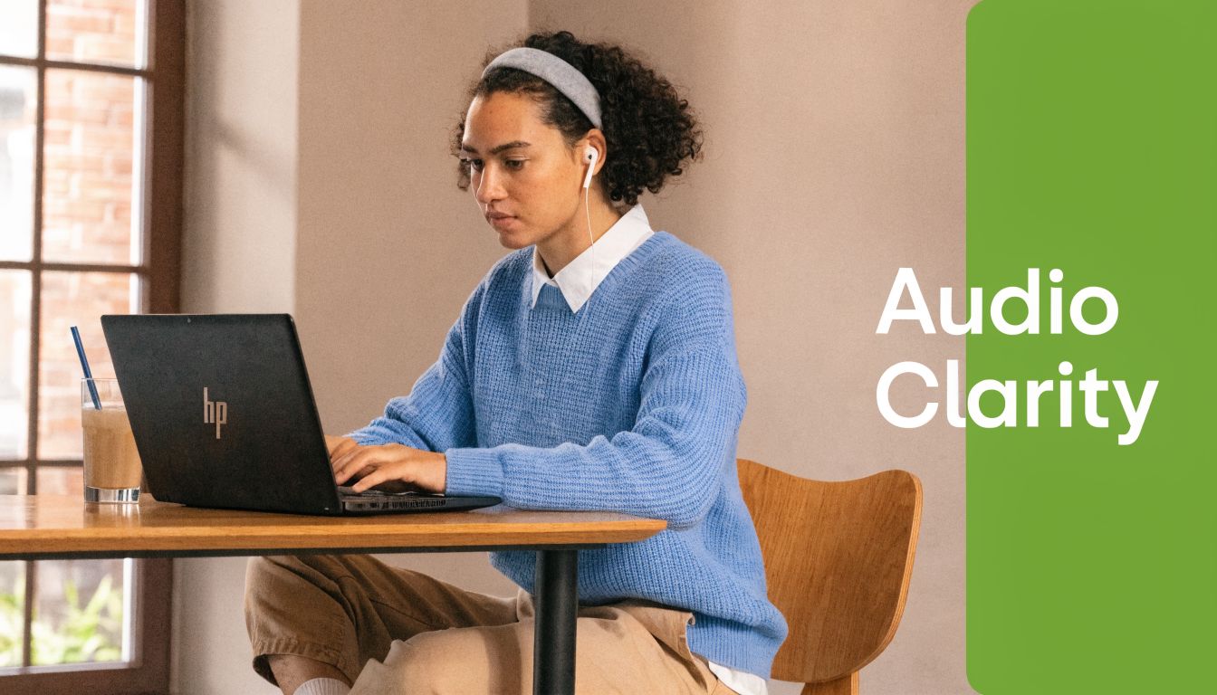 A woman wearing wired earbuds works on her HP laptop while sitting at a wooden desk.