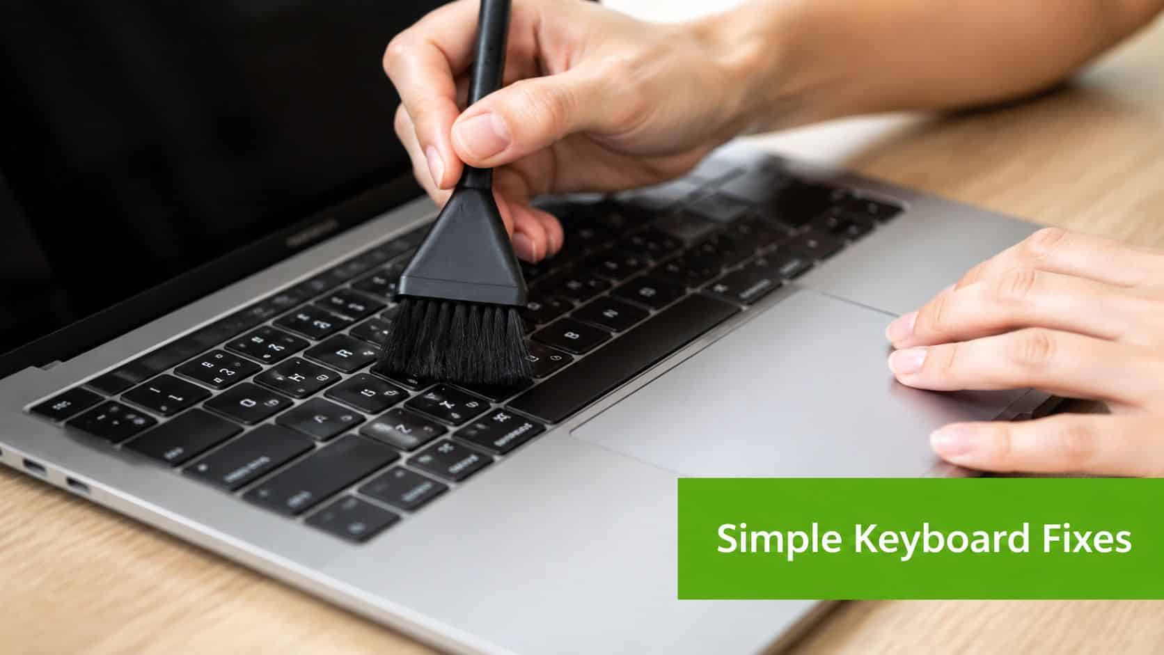 A person uses a small brush to clean debris from the keys of a modern laptop computer.