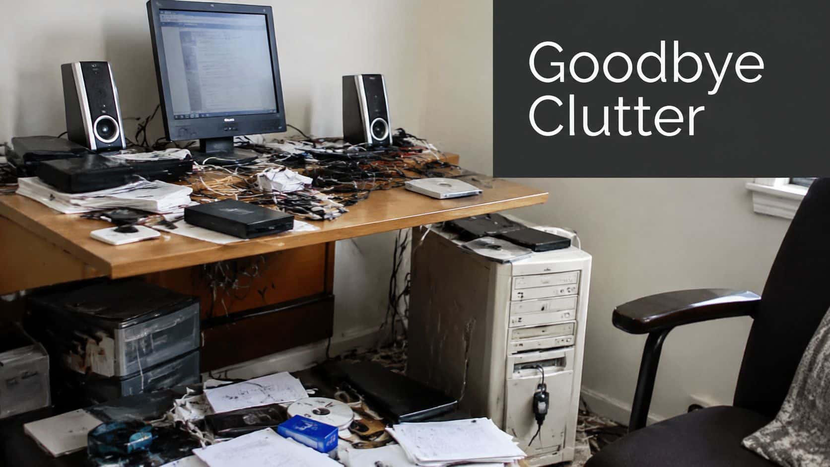 A messy office desk featuring a computer, tangled wires, documents, and computer components on a wooden surface.